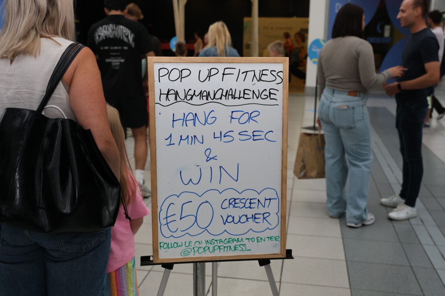 A handwritten sign reading Pop Up Fitness Hang Challenge, hang for 1 minute 45 seconds and win a 50 euro Crescent voucher.
